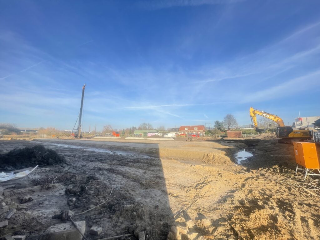 Bouwplaats met graafmachine en open grond onder een heldere blauwe hemel.