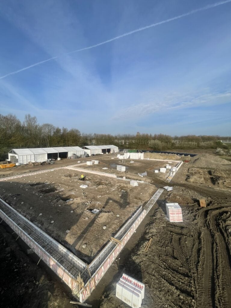 Fundering en bouwplaats onder een heldere blauwe hemel met wispy wolken.