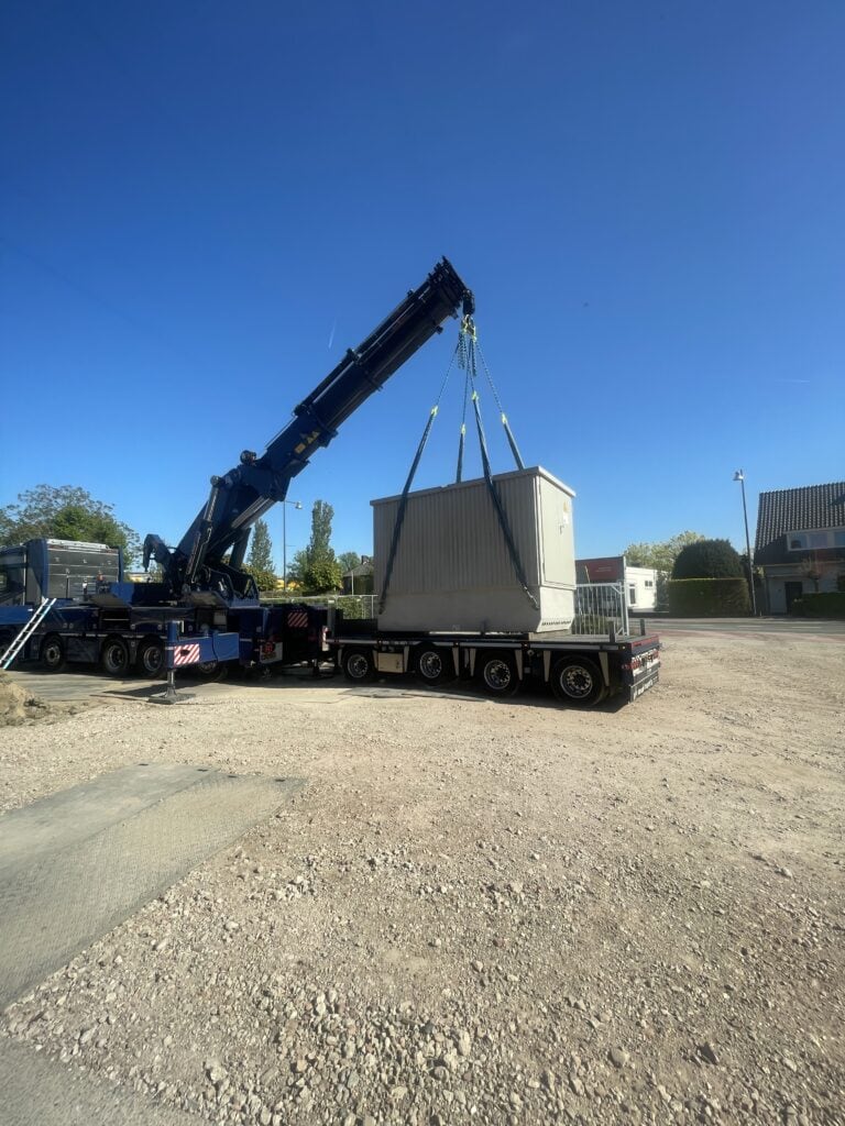 Afbeelding van hijskraan die een prefab betonnen fundering op een vrachtwagen plaatst.
