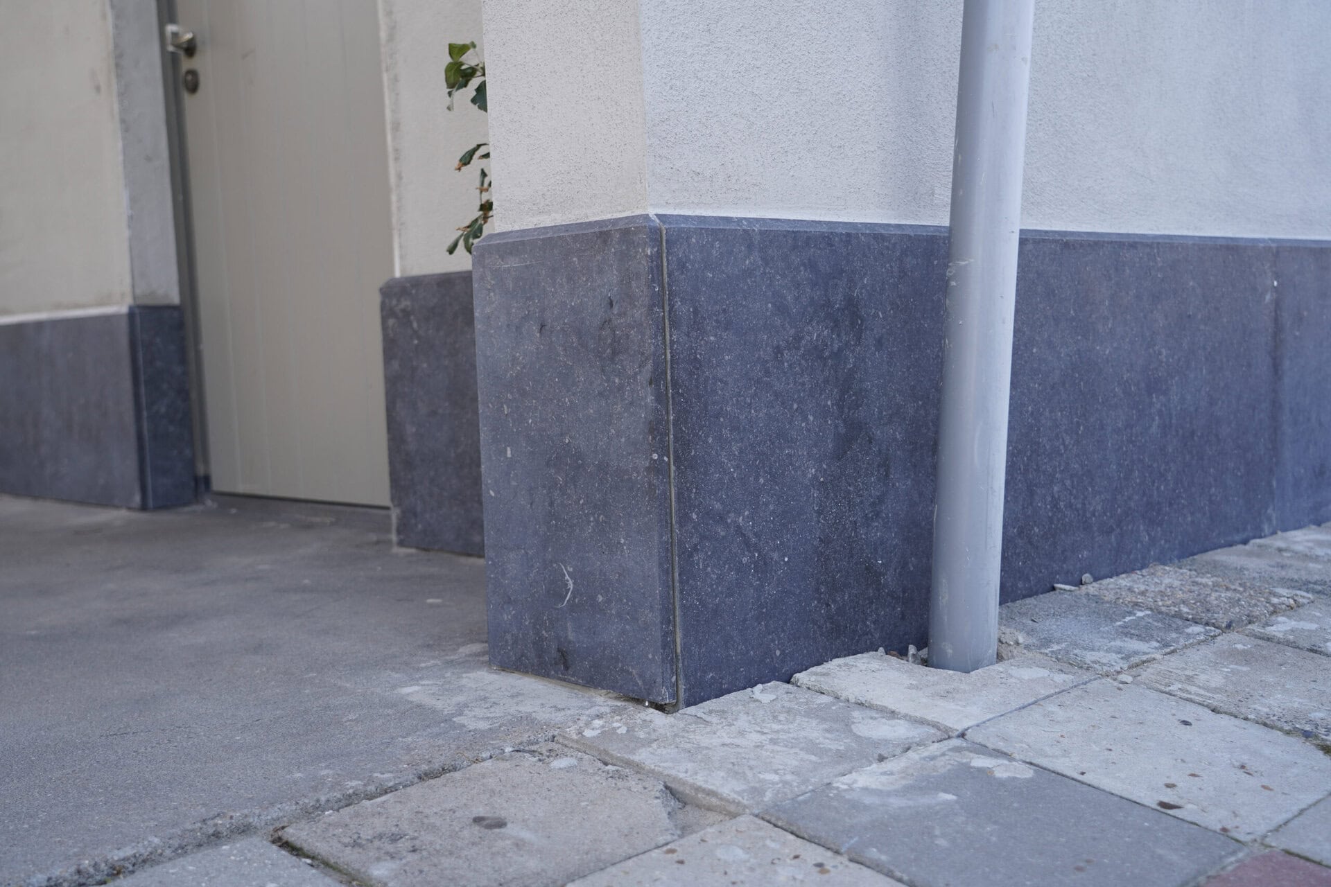 Pijlers en gevelafwerking met beton en steen, nabij deur en straat.
